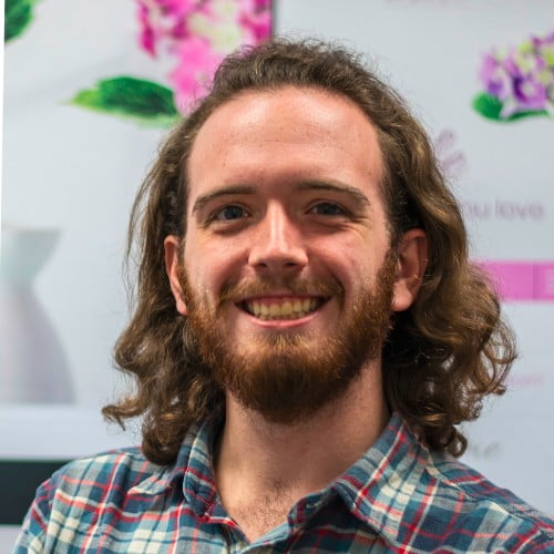 A picture of Blake Gambel, IT Consultant and founder of Gambel Labs. They have long brown hair, a short red beard, and are smiling at the camera.